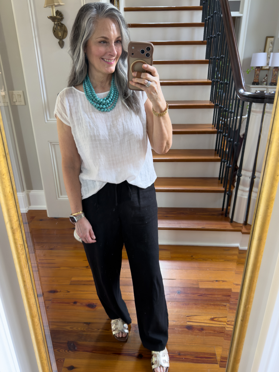 Woman wearing a white gauze top with black linen pants and turquoise necklace