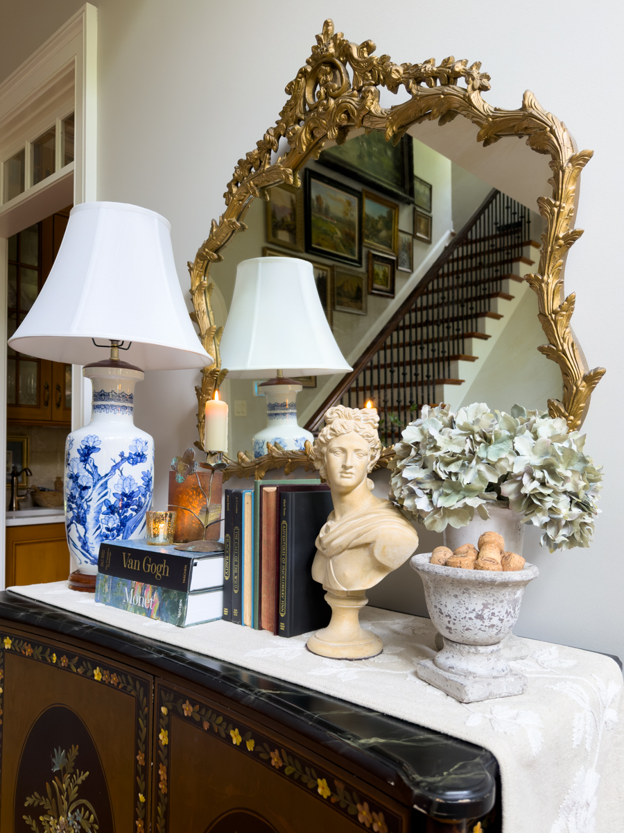 Summer to fall console table with blue and white lamp, vintage books, classical bust, hydrangeas, candles, and collected decor.