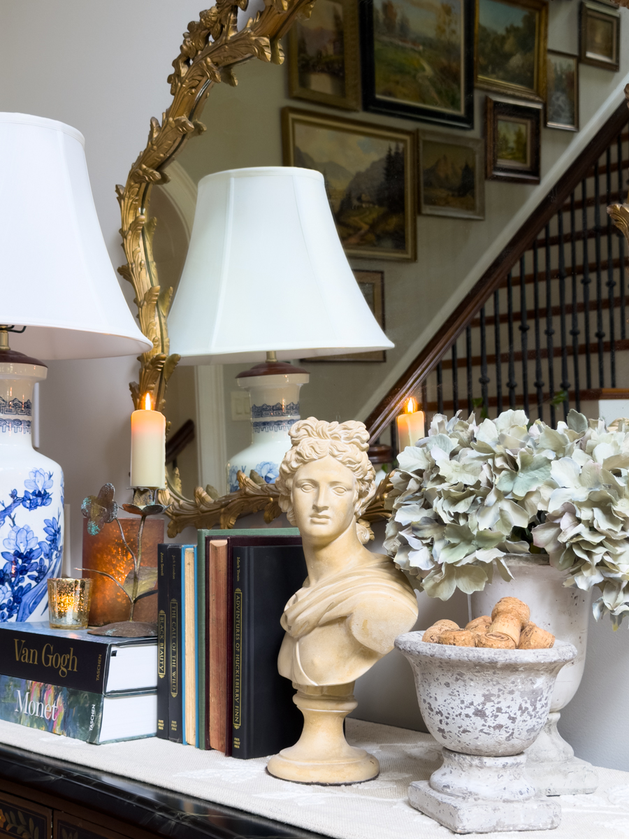 Close-up of a classical bust styled with vintage books, hydrangeas, warm candles, and collected decor for early fall.