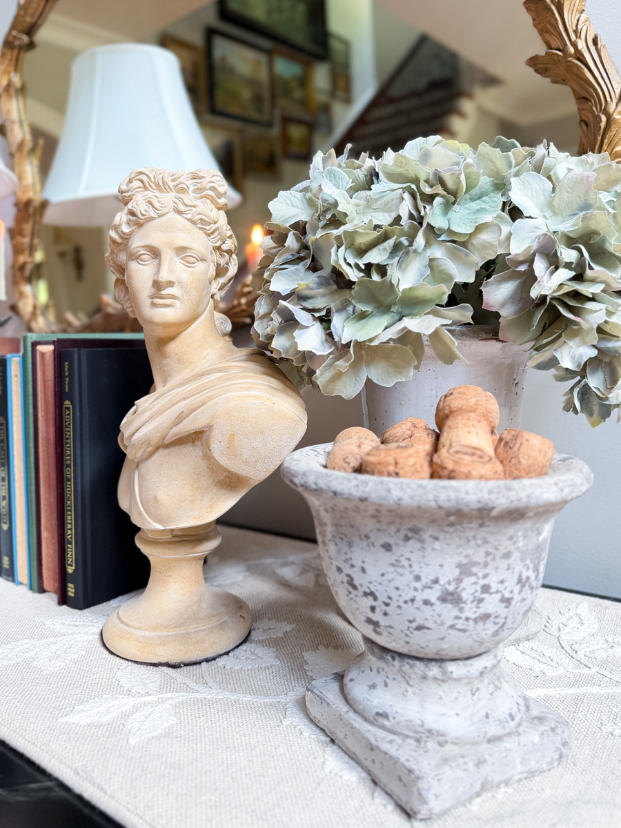 Classical bust beside faded hydrangeas and a stone urn filled with wine corks in a collected fall vignette.