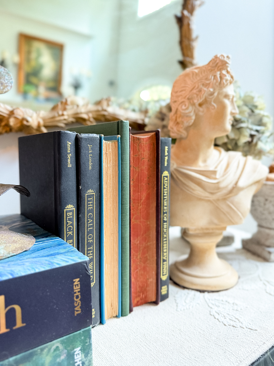 Vintage books in black, green, blue, and warm rust tones beside a classical bust for subtle early fall decorating.