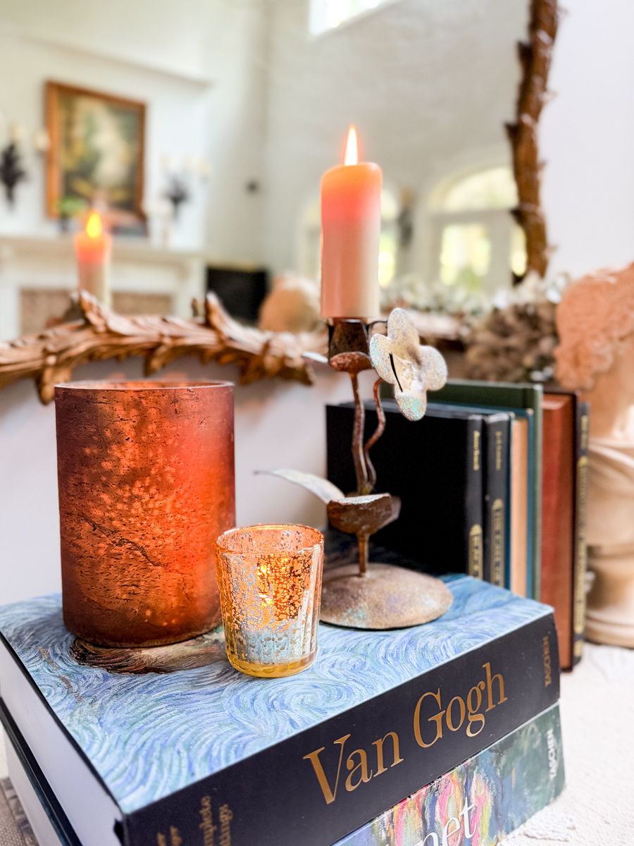 Glowing amber candleholders, vintage books, and metal flower candlestick styled for a subtle transition into fall.