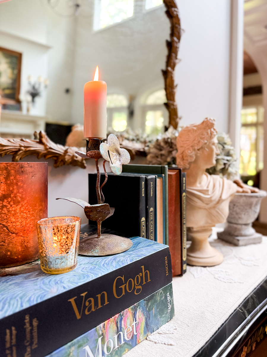 Warm amber candlelight, vintage books, and aged metal candlestick creating a cozy early fall vignette.