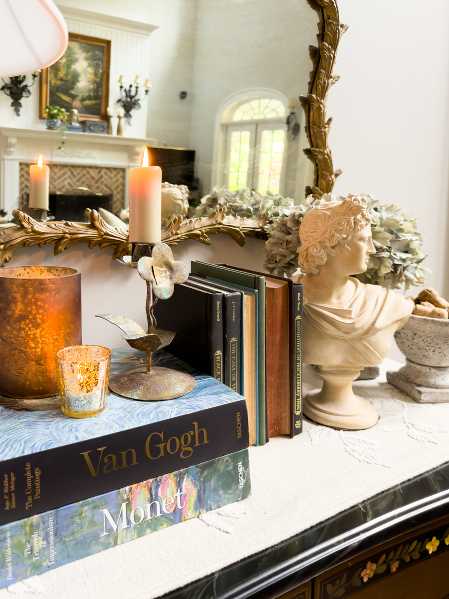 Van Gogh and Monet art books layered with candles, vintage books, and a classical bust in a collected fall display.