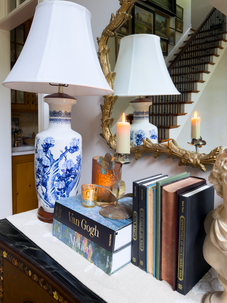 Blue and white lamp styled with art books, candles, and vintage books for a subtle summer to fall transition.