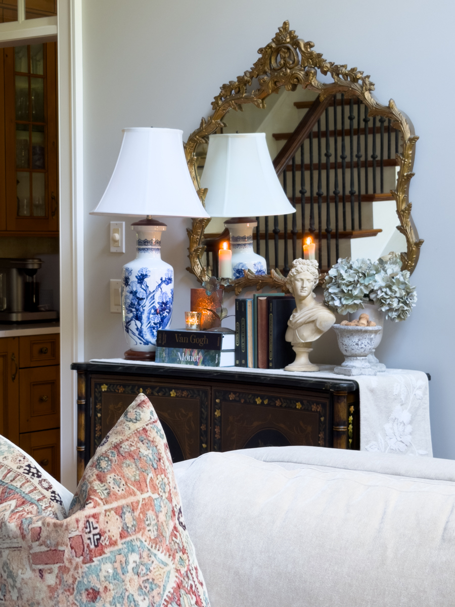 Traditional living room with a painted cabinet styled with blue and white lamp, gold mirror, books, candles, and hydrangeas.