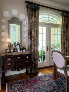Antique wood chest styled as a home bar beside French doors and patterned drapes