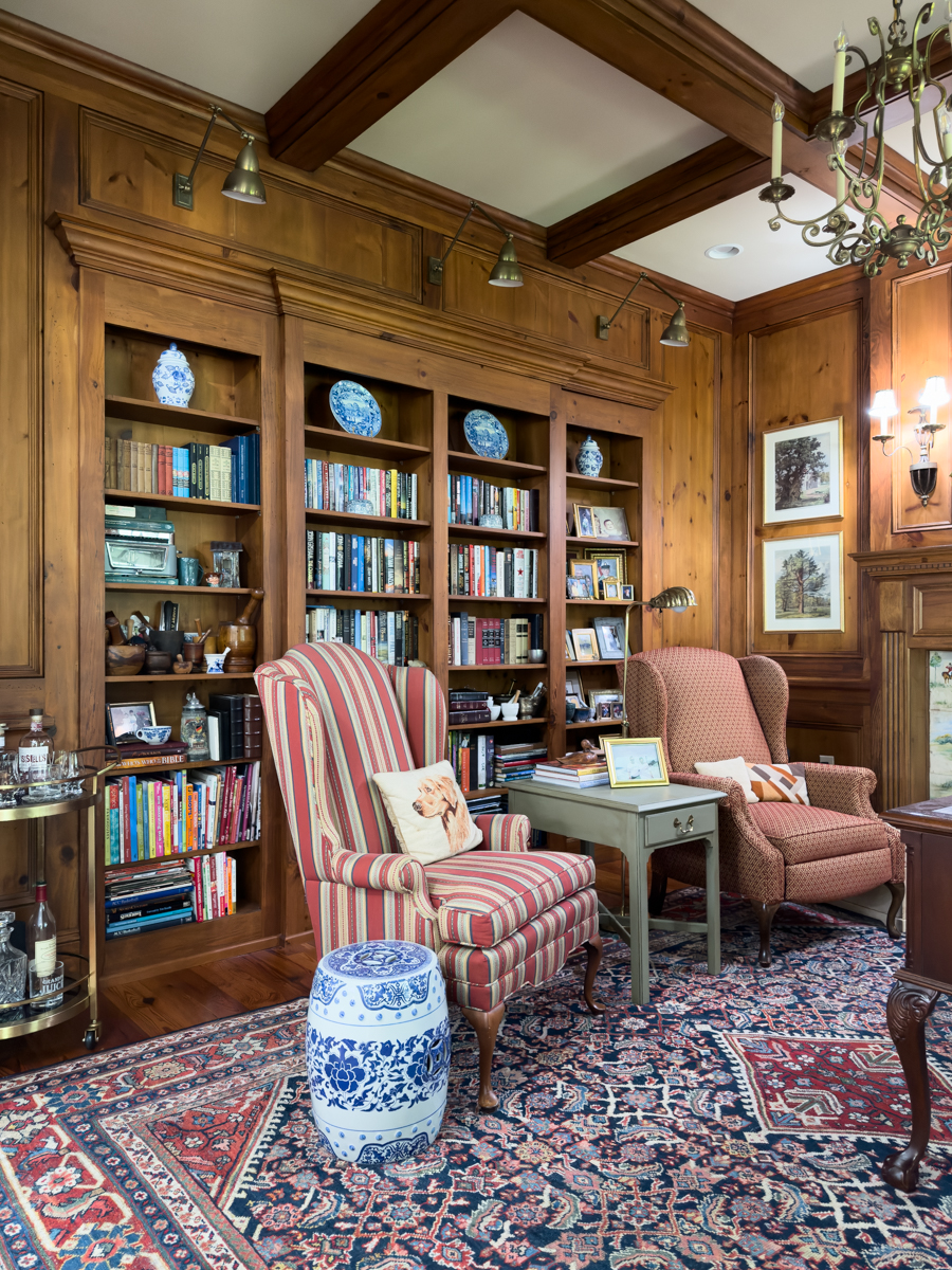 Traditional wood-paneled den before the furniture update with two mismatched chairs and built-in bookcases