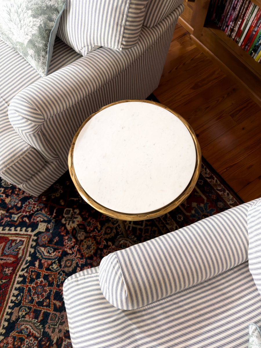 Round marble-top and brass side table between two blue and white striped chairs