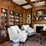 Cozy traditional den with striped chairs, built-in bookcases, wood paneling, fireplace, and patterned rug
