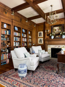 Cozy traditional den with striped chairs, built-in bookcases, wood paneling, fireplace, and patterned rug
