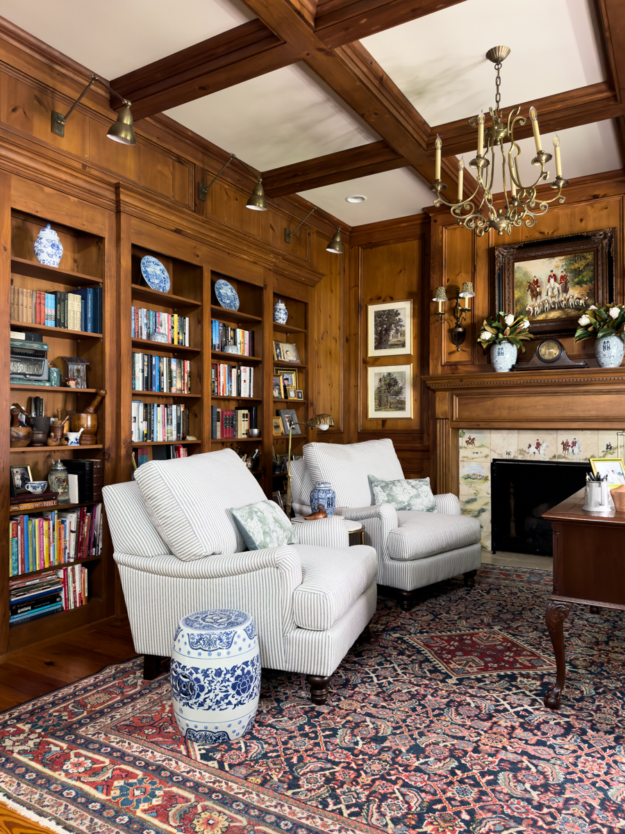 Cozy traditional den with striped chairs, built-in bookcases, wood paneling, fireplace, and patterned rug
