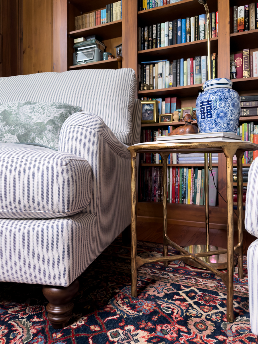 Marble and brass side table styled with books and a blue and white ginger jar beside a striped chair