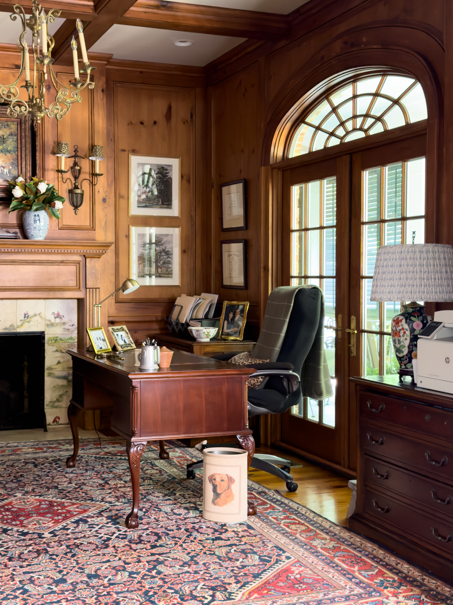 Wood-paneled fireplace with equestrian artwork, decorative tile, blue and white vases, and brass sconces