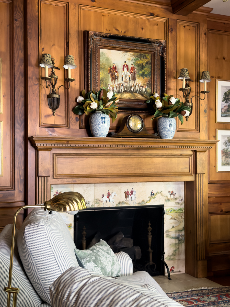 Traditional wood fireplace with equestrian tile, blue and white vases, artwork, and striped reading chair