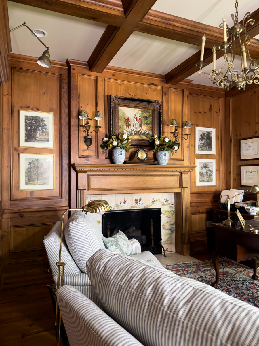 Traditional wood-paneled den combining a home office, fireplace, and striped reading chairs