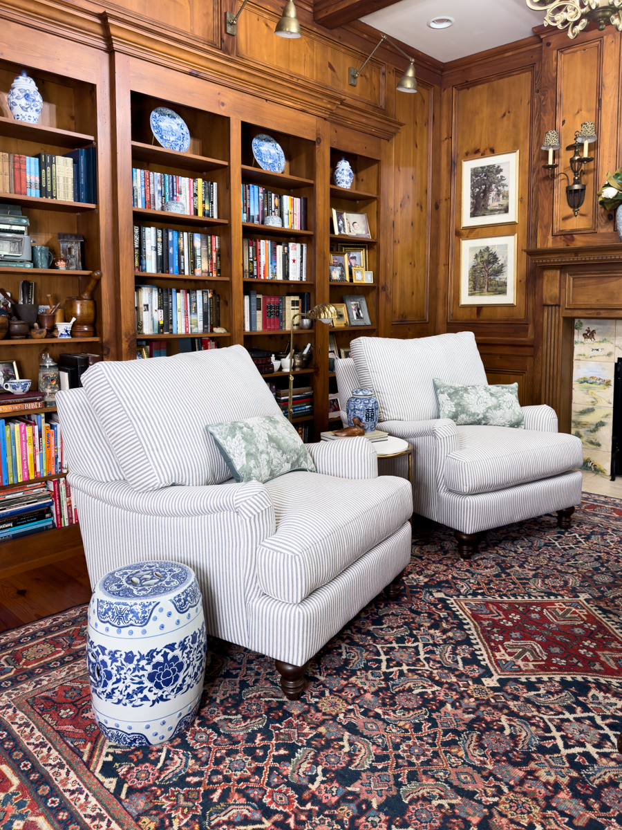 Two striped chairs in a traditional wood-paneled den with built-in bookcases and patterned rug
