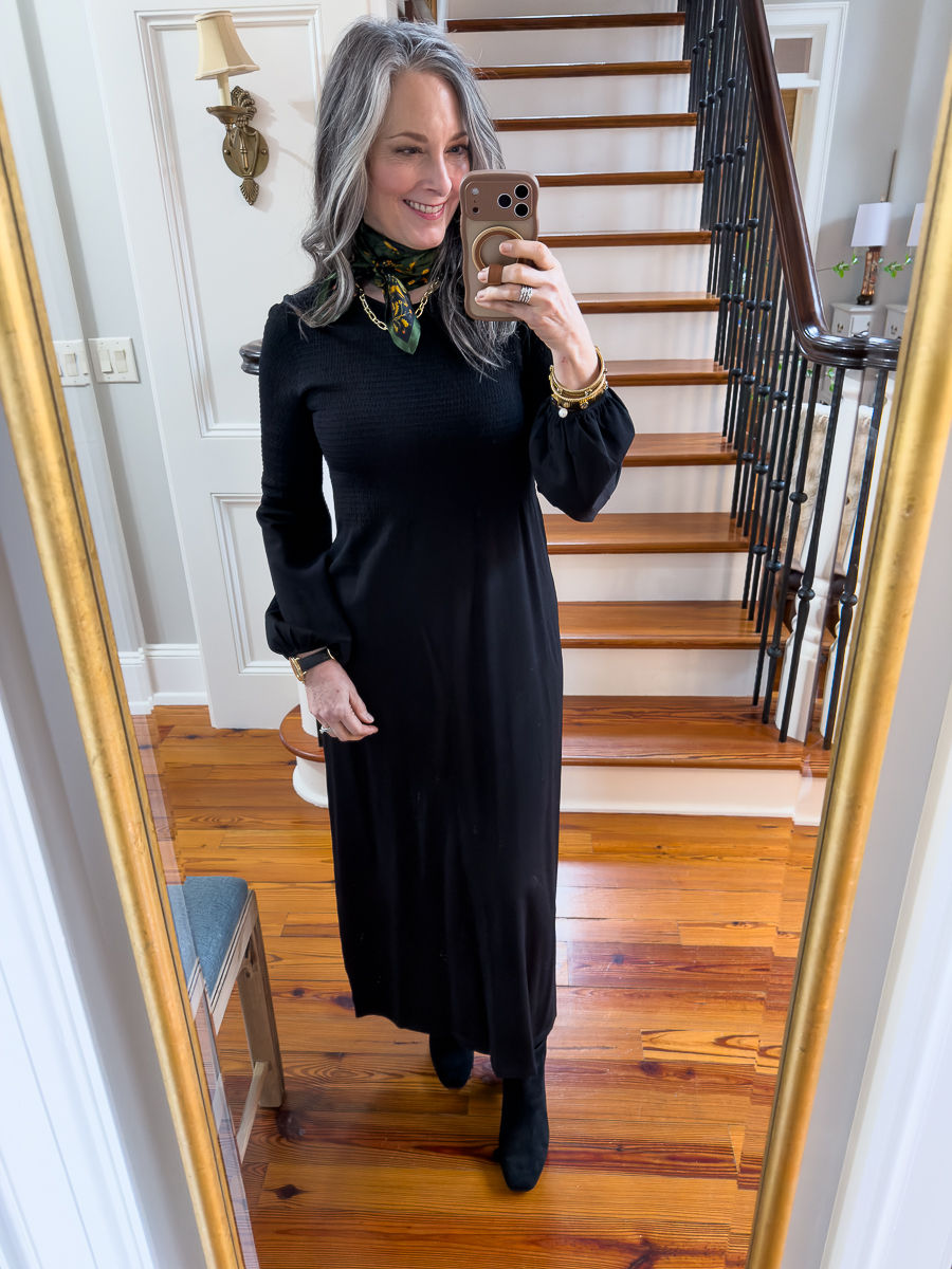 Woman wearing a black midi dress styled with a scarf, taking a mirror selfie indoors.