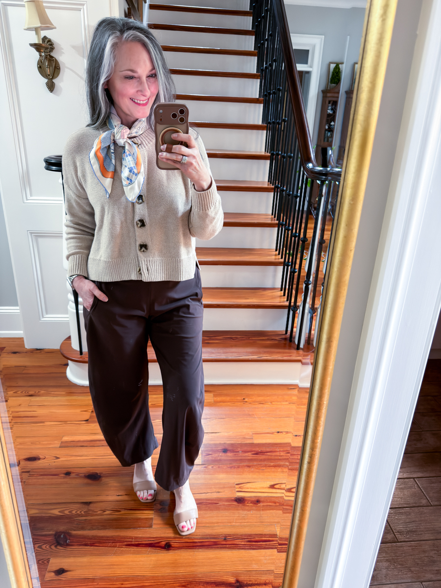 Woman wearing beige cardigan, brown pants, and silk scarf in mirror selfie