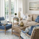 Nancy Meyers inspired sunroom featuring Benjamin Moore Chantilly Lace walls, tan sofa, wicker chairs with blue block print cushions, green trimmed linen curtains, and brass accents.