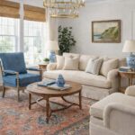 Classic living room with Benjamin Moore Wind’s Breath walls, coral patterned rug, blue accent chair, chinoiserie lamps, and neutral upholstered sofa