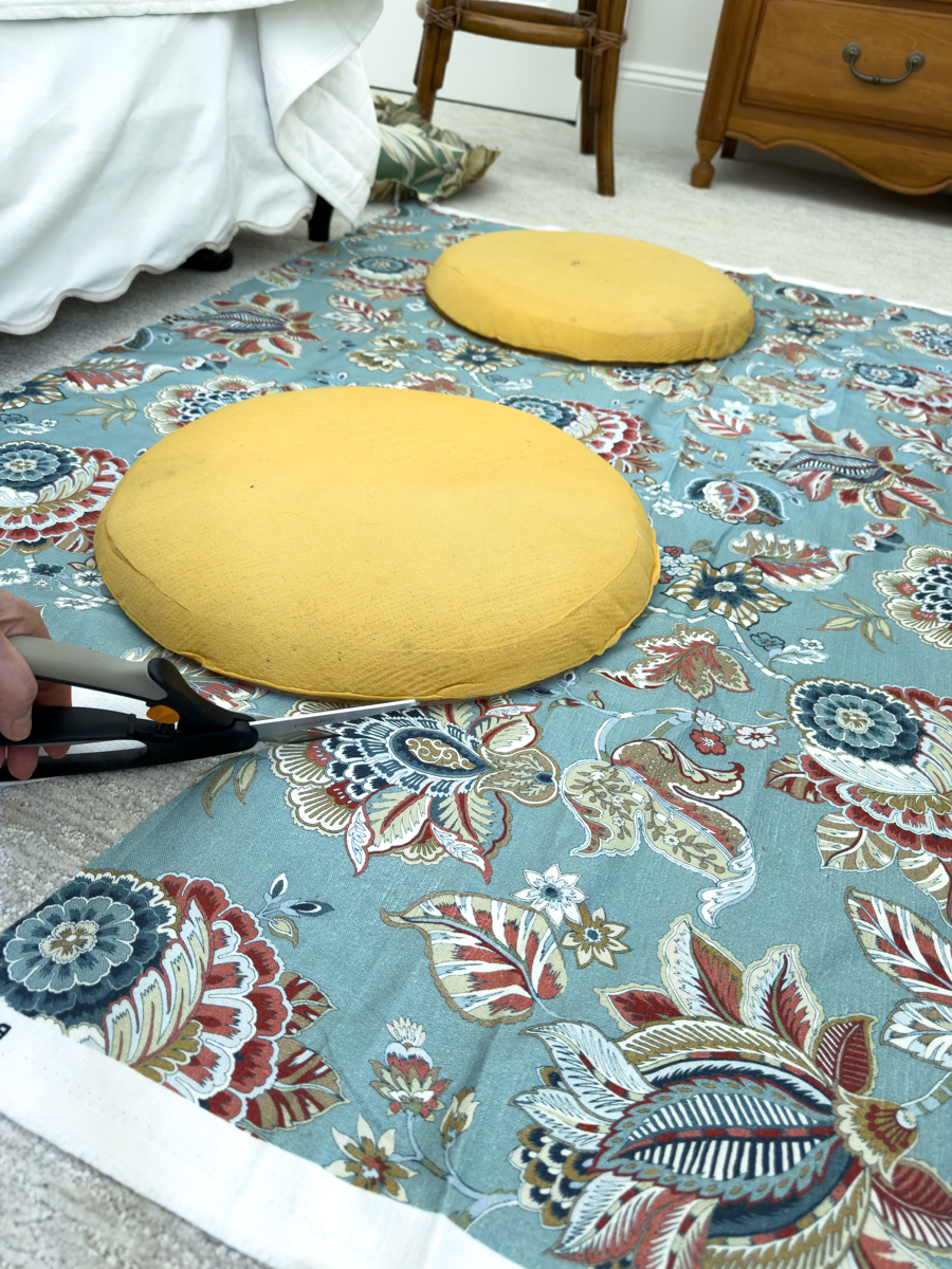 Round chair cushions placed on blue floral upholstery fabric while cutting new fabric for the seats.