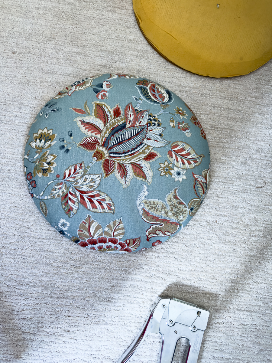 Finished round chair seat recovered in blue floral upholstery fabric beside the original seat cushion.