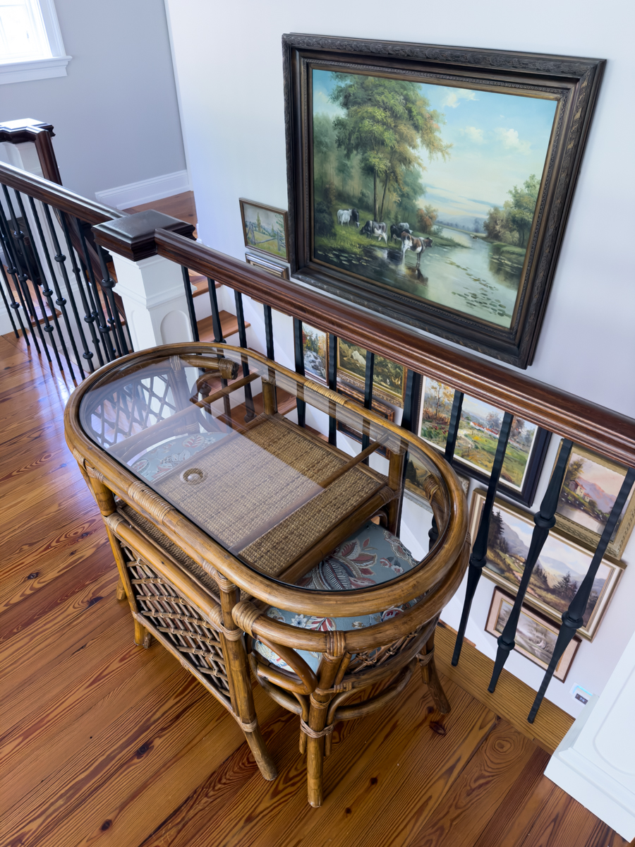 Rattan table and chairs on an upstairs landing beside a collected gallery wall of landscape paintings.