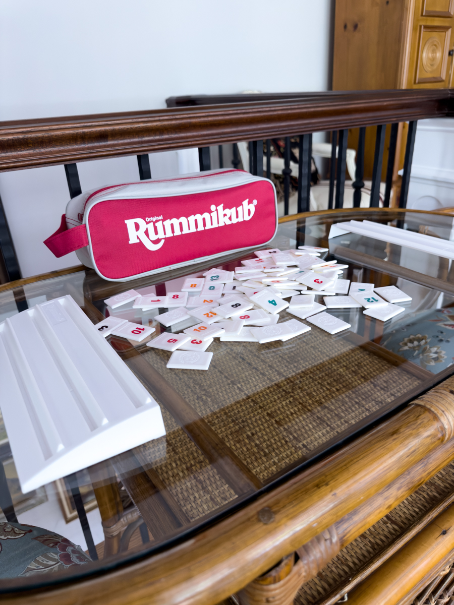 Rummikub tiles and game racks arranged on the glass top of a rattan table.