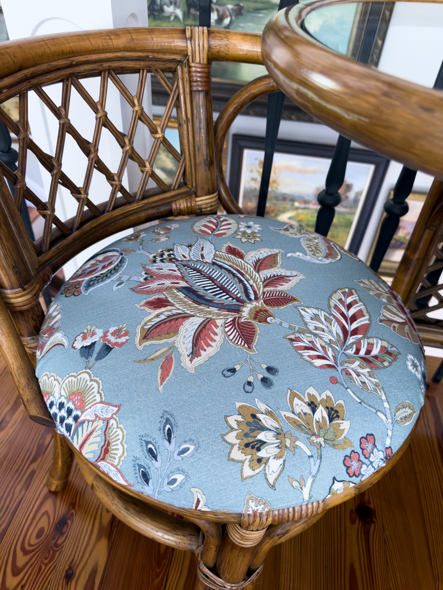 Close-up of blue floral upholstery fabric on the round seat of a brown rattan chair.