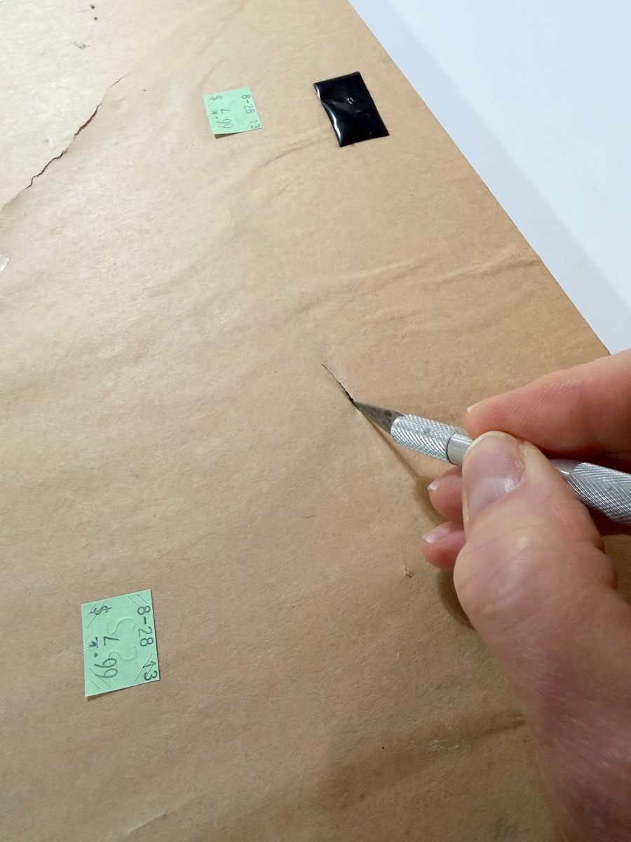 Cutting open brown paper backing on thrifted frame with craft knife