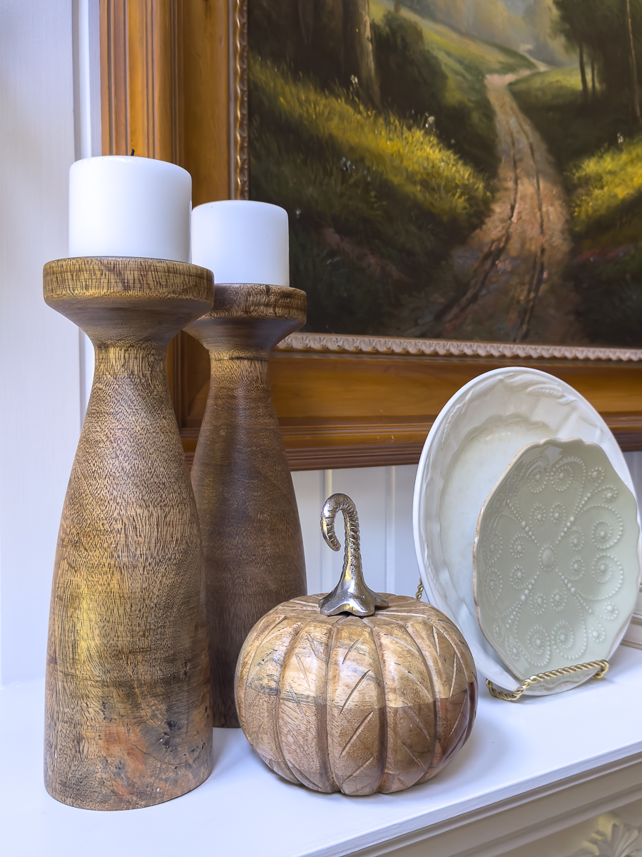 Decorative plate, wooden pumpkins, and two wooden candlesticks with white candles on a mantel.