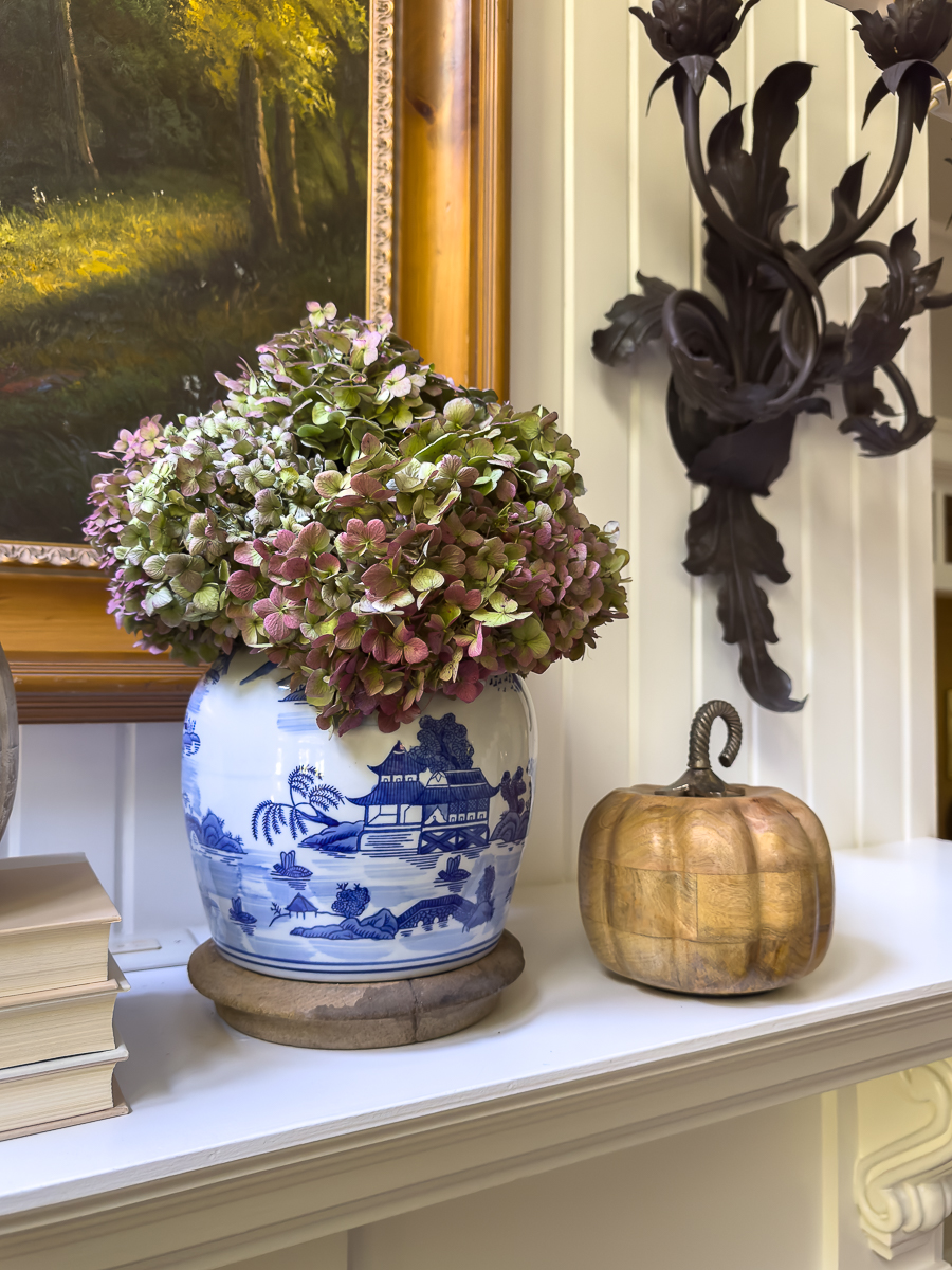 A chinoiserie vase with dried hydrangeas styled on a fall mantel with wooden pumpkins.