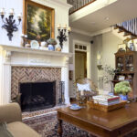 A cozy fall living room with a brick fireplace, classic artwork, and a decorated mantel featuring chinoiserie, pumpkins, and dried hydrangeas.