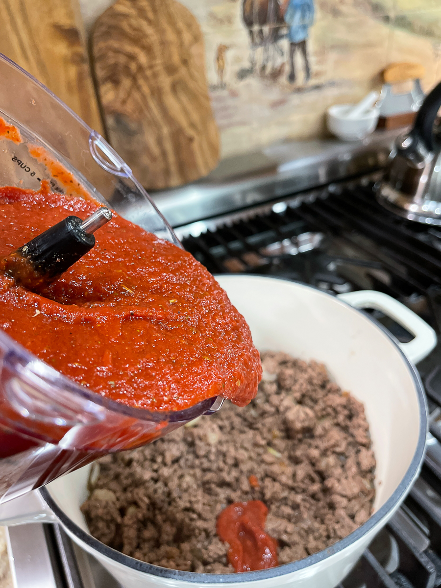 pouring tomato sauce into ground beef