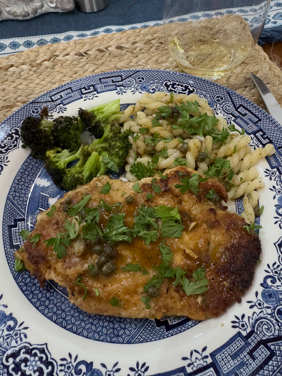 Plate of chicken piccata with broccoli and pasta on a blue and white plate.