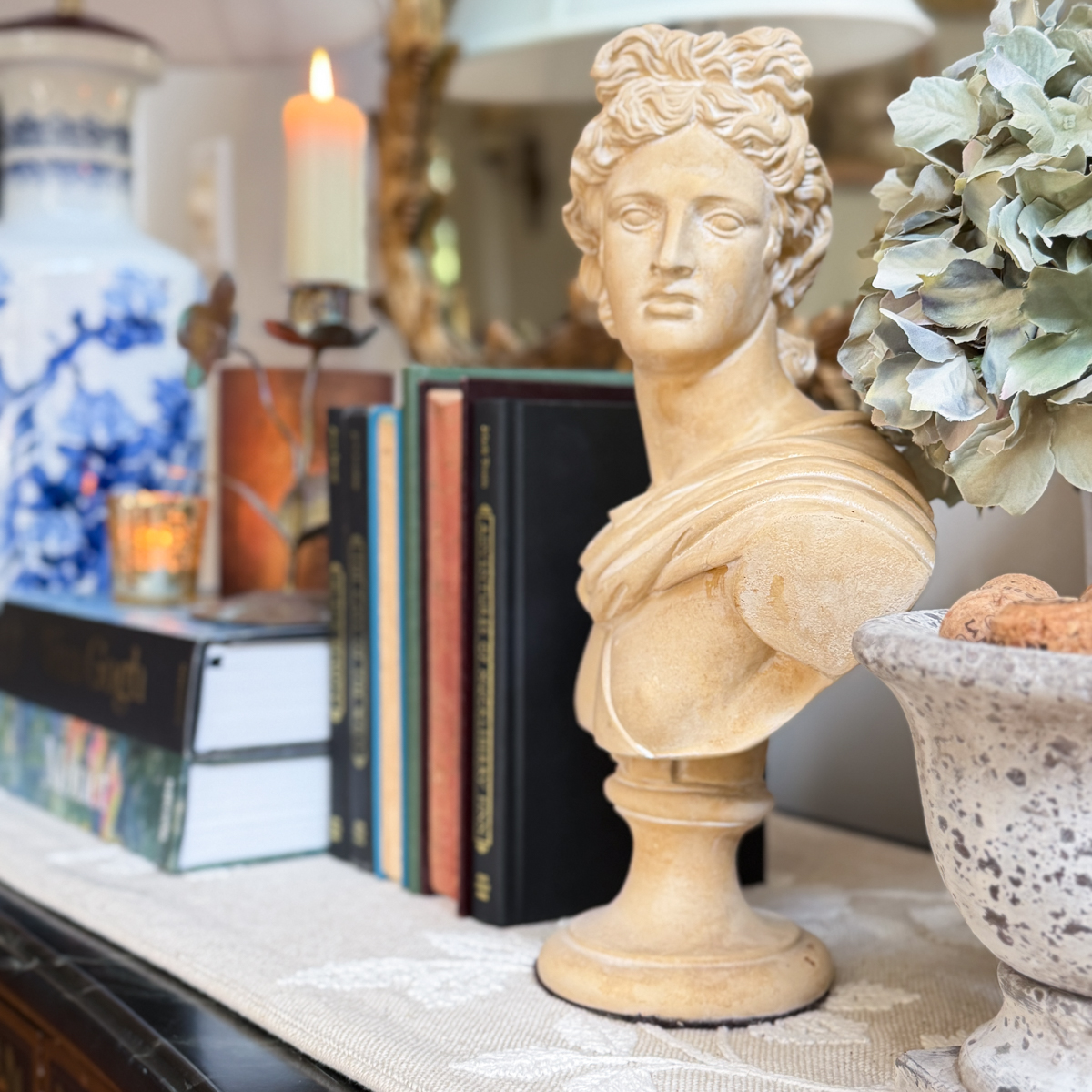 Classical bust surrounded by vintage books, faded hydrangeas, candlelight, blue and white decor, and a weathered urn.