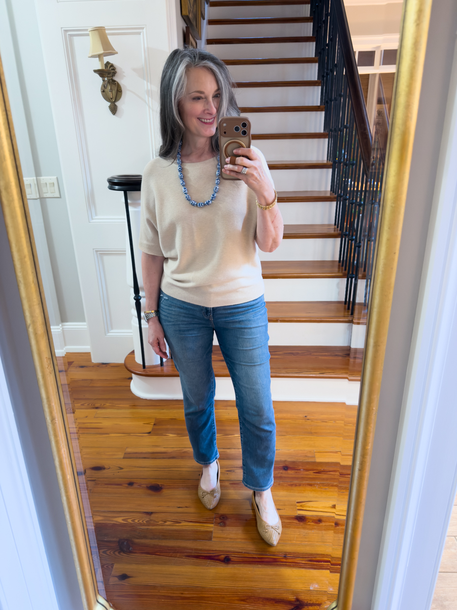Woman wearing a neutral batwing sweater with blue jeans and pointed ballet flats in mirror selfie