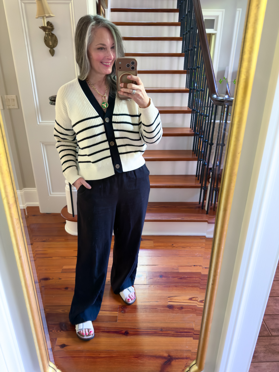 Woman wearing a black and white striped cardigan with black wide leg pants and white sandals