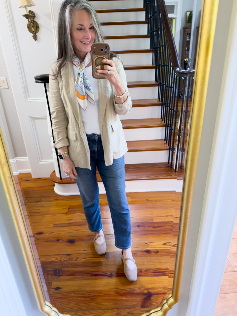 Woman wearing a beige linen blazer with jeans, white top, and printed silk scarf