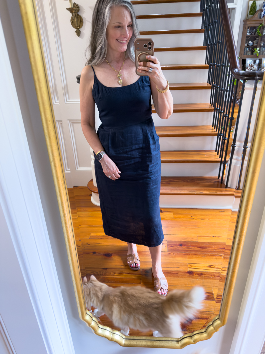 Woman wearing a navy linen midi dress with neutral sandals in mirror selfie