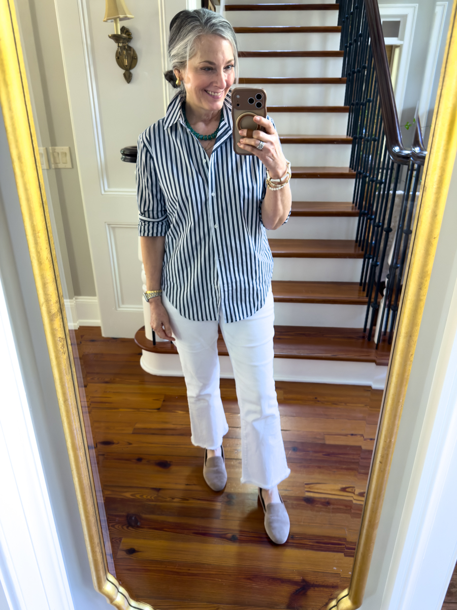 Woman wearing a blue striped button down shirt with white cropped jeans and loafers