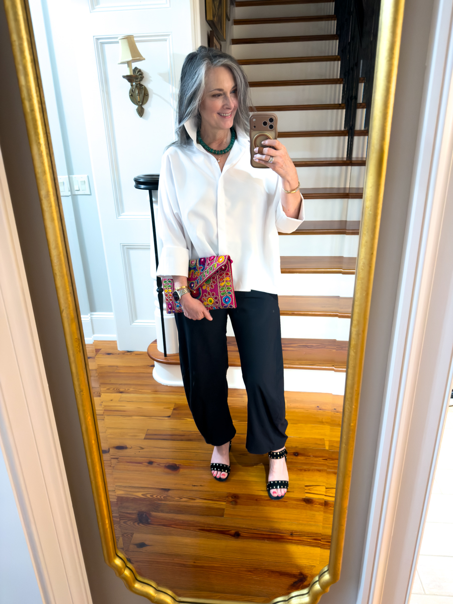 Woman wearing oversized white shirt with black wide leg pants and colorful clutch bag