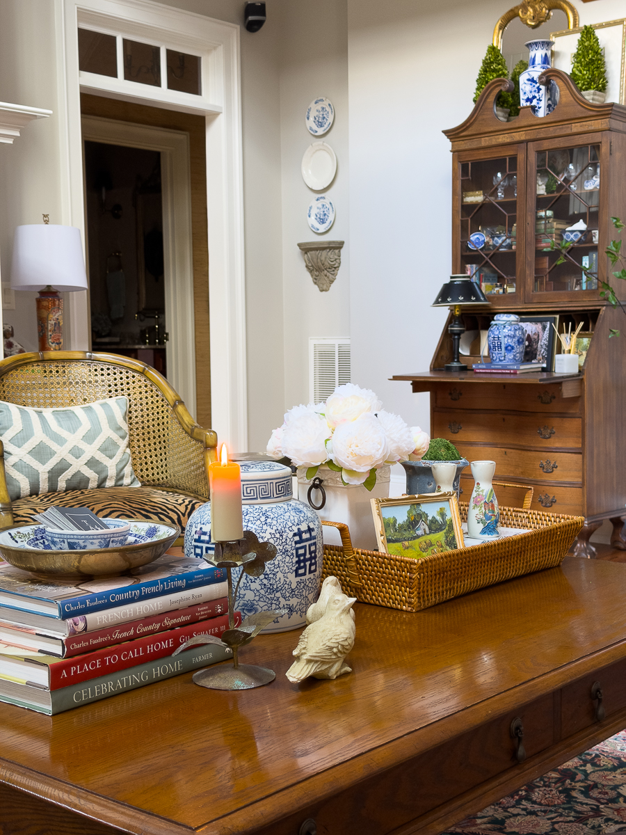 Layered coffee table styling with thrifted books, ginger jar, candlestick, tray, and flowers.