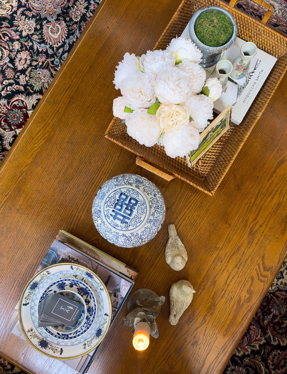 Overhead view of a coffee table styled with thrifted decor, books, bowls, tray, and flowers.