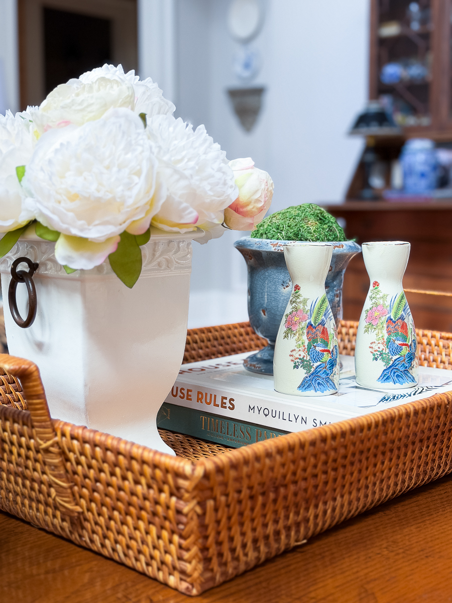 Wicker tray styled with thrifted urn, sake pitchers, books, and flowers on a coffee table.