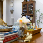 Classic wooden coffee table styled with thrifted decor including books, ginger jar, tray, flowers, and vintage accessories.