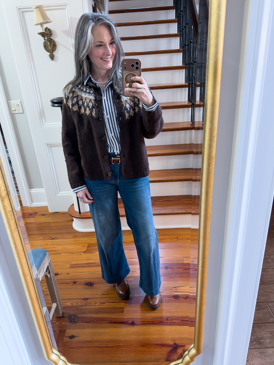 Woman wearing a brown Fair Isle cardigan with a striped shirt and jeans, taking a mirror selfie.
