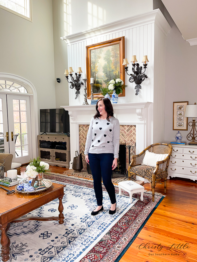 lady wearing a heart sweater in front of a fireplace