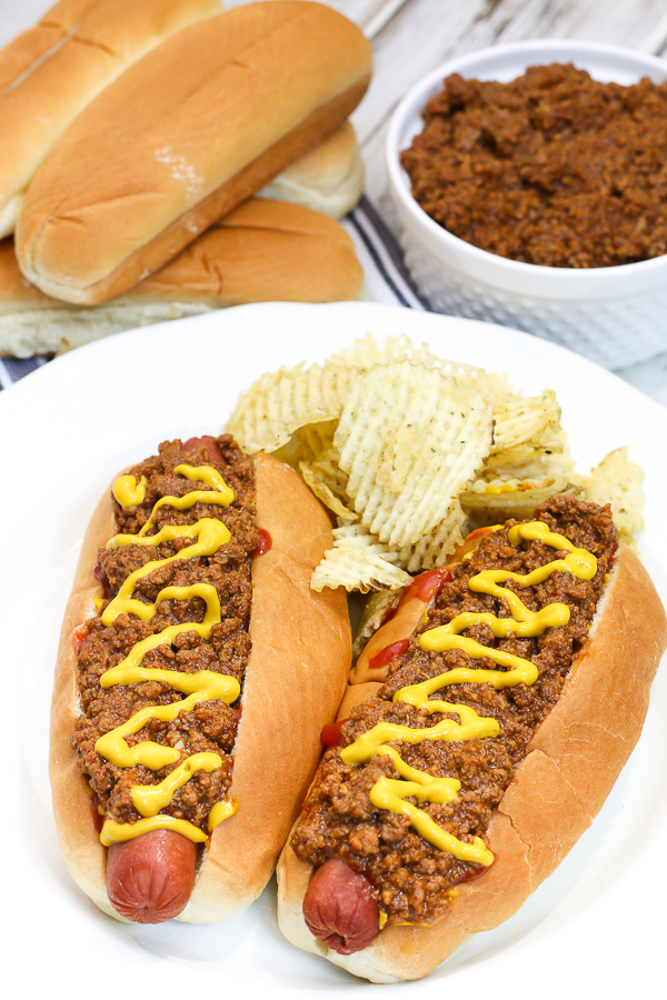 hot dogs with chili and mustard with chips on a white plate